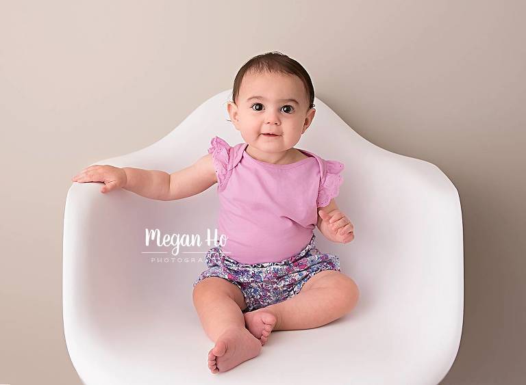 happy smiling toddler girl in pink and flower shorts in chair during studio session in southern nh