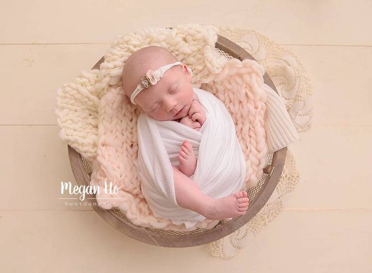 wrapped little baby girl in white in little bowl on wood floor