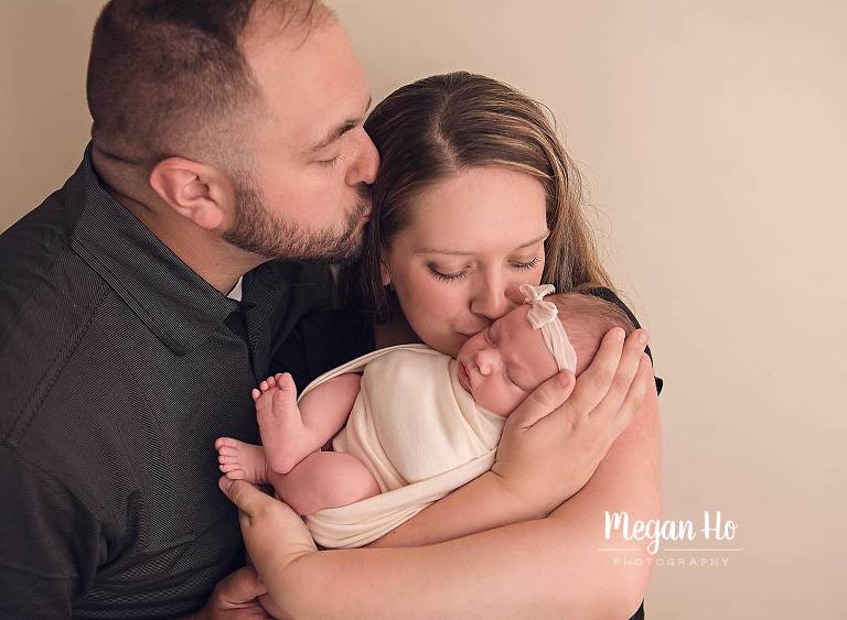 proud new parents kissing with wrapped baby girl in New Hampshire studio session