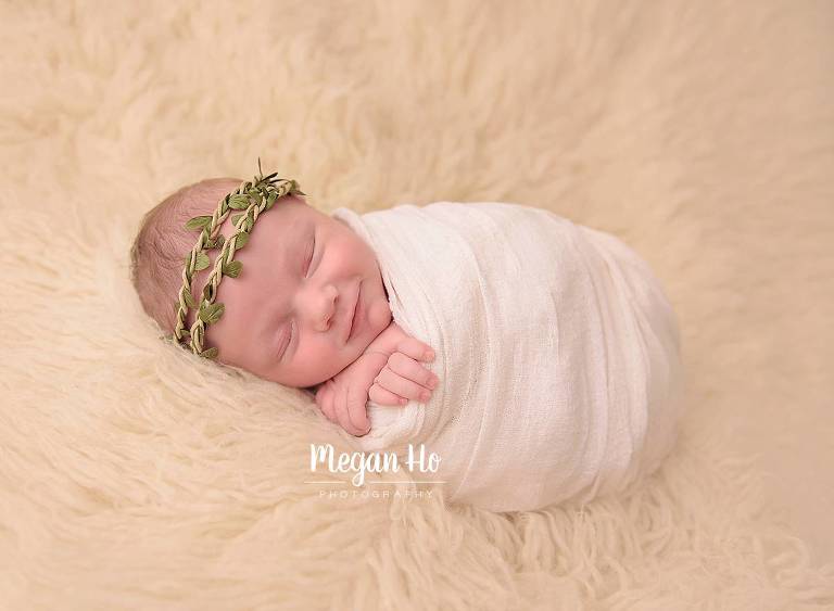 smiling little girl wrapped in white with green halo sleeping during studio session in new hampshire