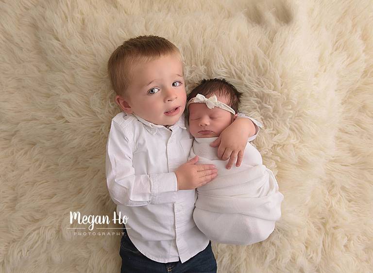 big brother snuggling with baby sister on white fluffy rug southern nh newborn session