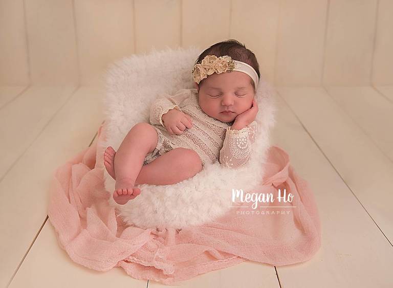 little newborn girl in pretty lace romper sitting in little white chair