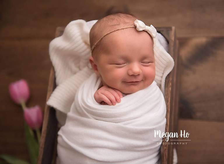 smiling little baby girl wrapped in white with tulips new hampshire