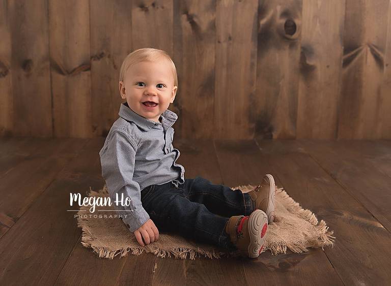 happy little boy in blue sitting on wood floor