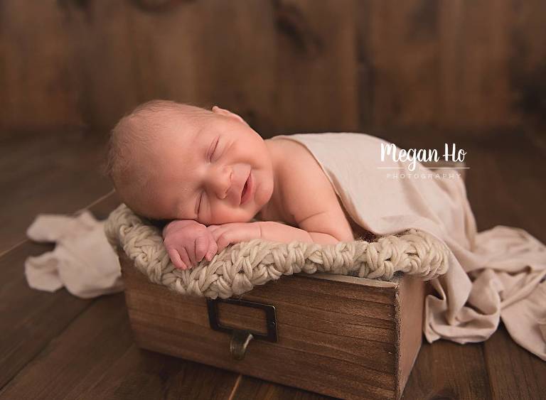 newborn baby boy sleeping in wooden drawer smiling