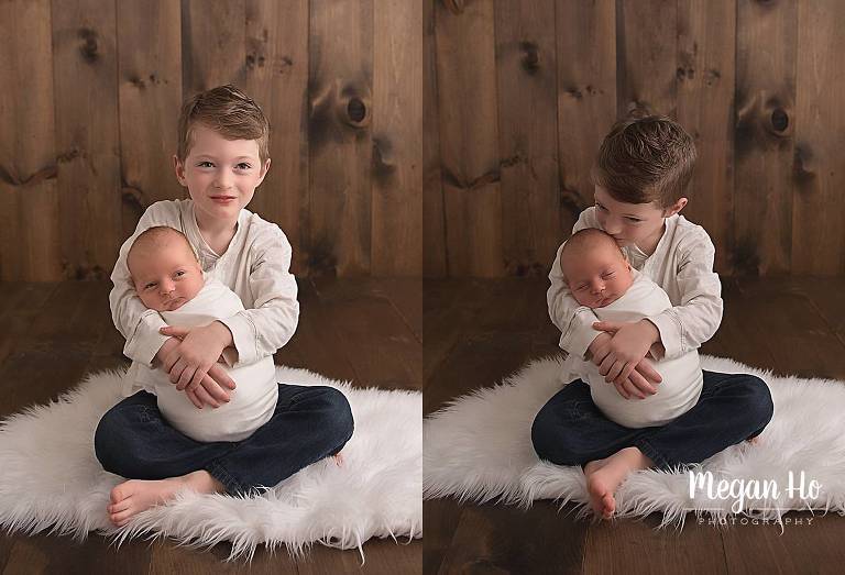 big brother sitting holding newborn boy on white rug
