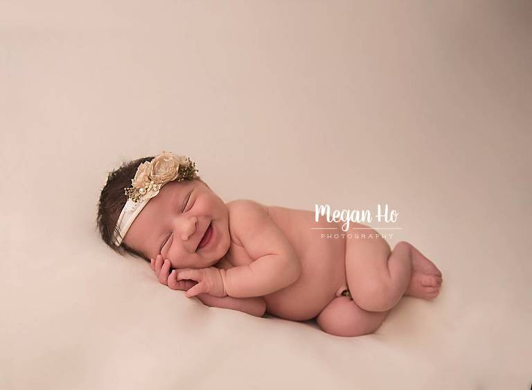 smiling baby girl sleeping on white backdrop in newborn session