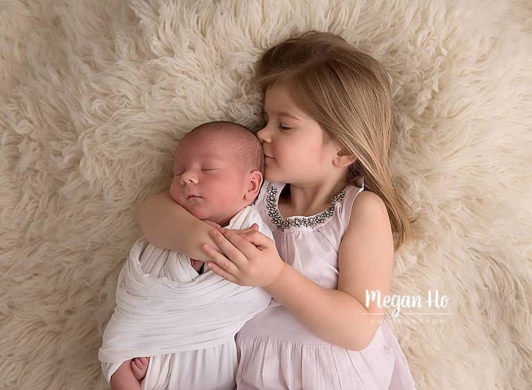big sister holding and kidding wrapped newborn baby brother in nh newborn session