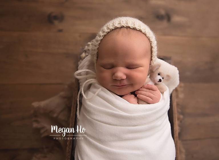 newborn baby boy snuggling with small teddy bear in studio