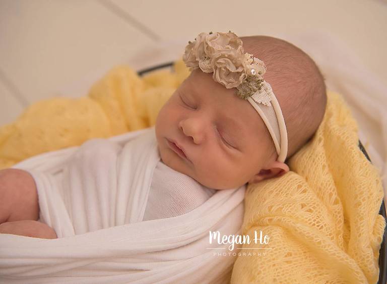 newborn baby girl swaddled in bowl on yellow blanket