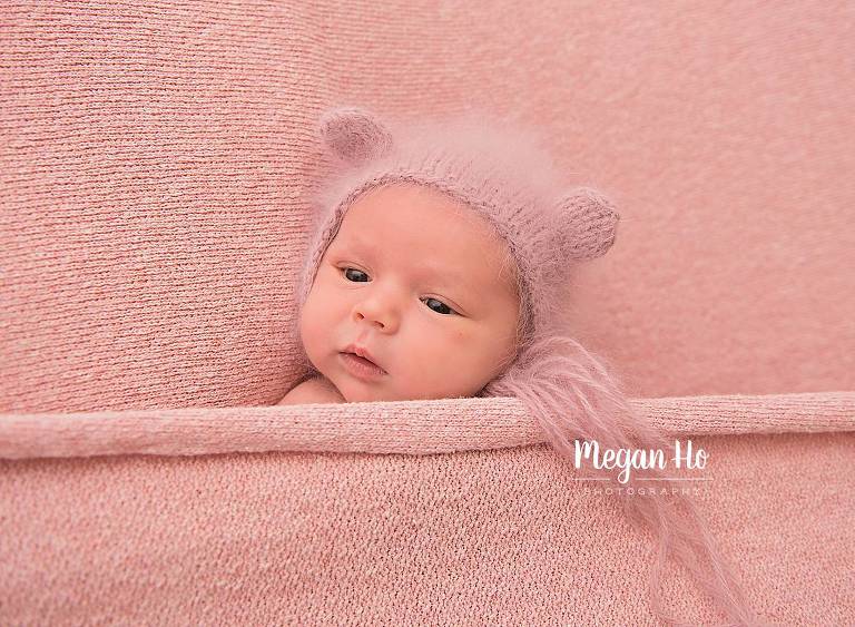 adorable little baby girl in bear hat snuggled in pink blankets