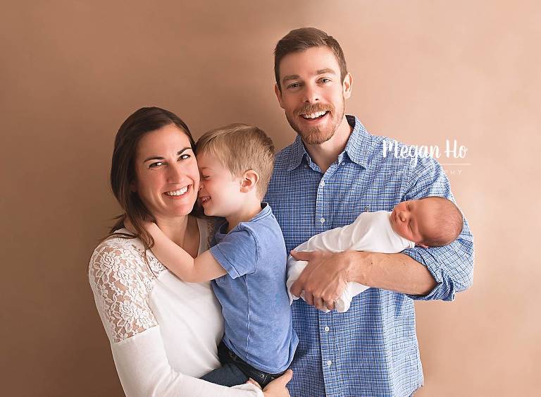 big brother laughing with mom while dad snuggles baby boy in newborn session
