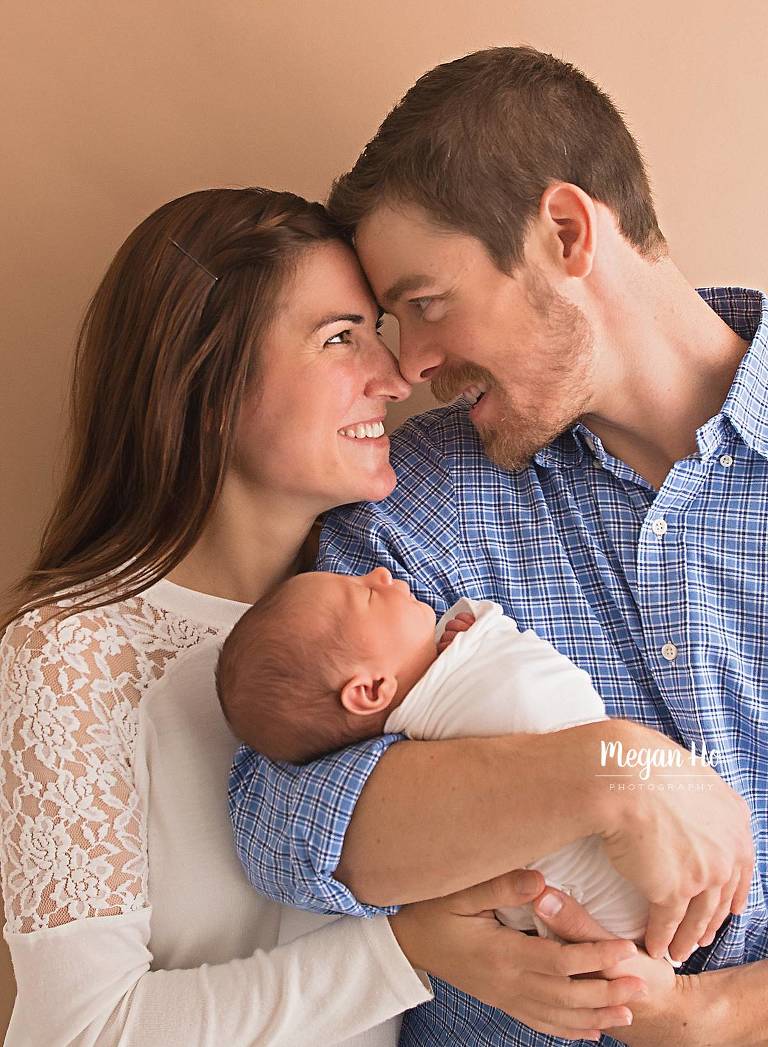 mom and dad look into each others eyes holding newborn baby