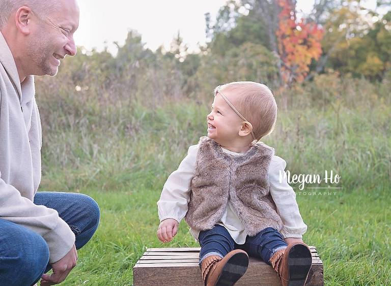 little girl sitting on a crate smiling at dad in nh family session