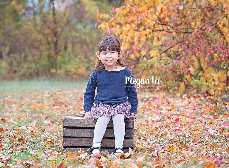little girl sitting on crate with fall leaves all around