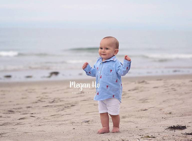 happy boy in lobster shirt walking along beach at one year photo session
