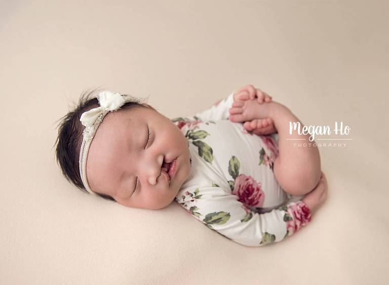 newborn girl in flower onesie sleeping while holding her foot southern nh
