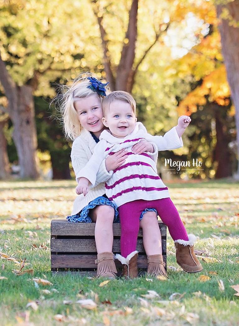 sisters snuggling while sitting on crate in fall family session