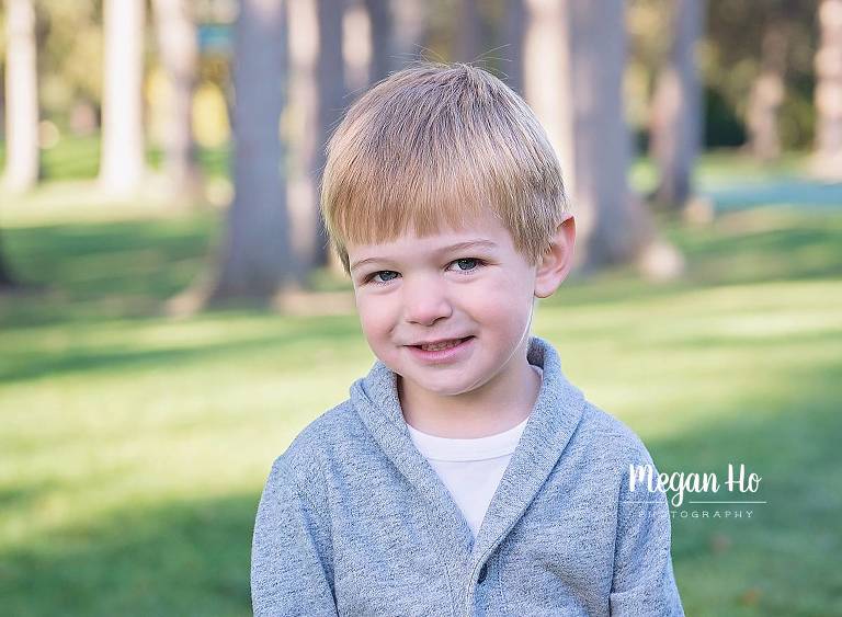 three year boy with grey sweater sitting and smiling in park