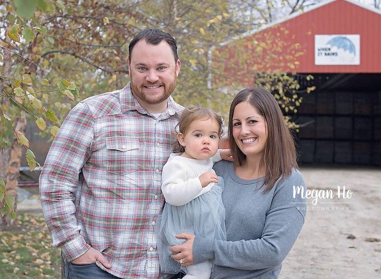 family of three in front of red barn in nh fall session