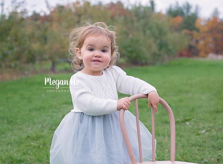 adorable smiling girl in white tutu sweater dress holding chair in nh apple orchard