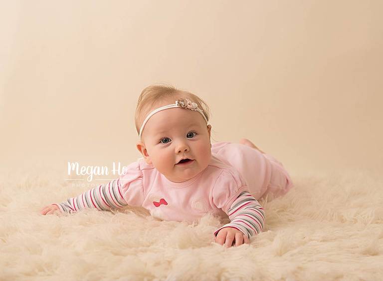 adorable girl in nh studio laying on fuzzy cream rug for four month session