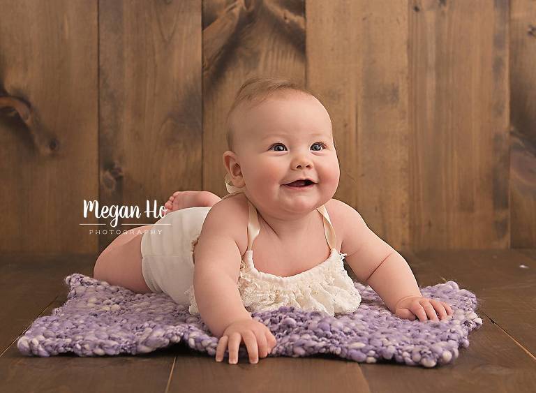 little girl in white romper laying on belly on purple bump blanket