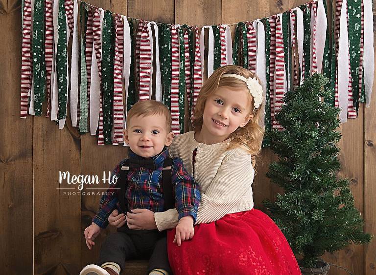 holiday studio session brother and sister sitting on wood with Christmas tree