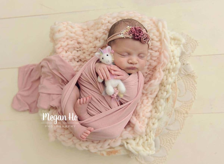 newborn girl wrapped in pink snuggling unicorn on white wood floor bedford nh