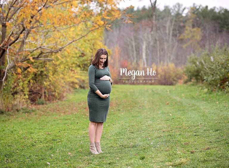 mom to be looking down at her belly in tight green dress in apple orchard