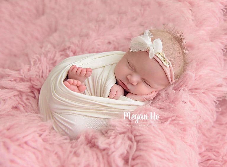 baby girl wrapped in white wrap snuggled on pink fluffy rug sleeping in nh