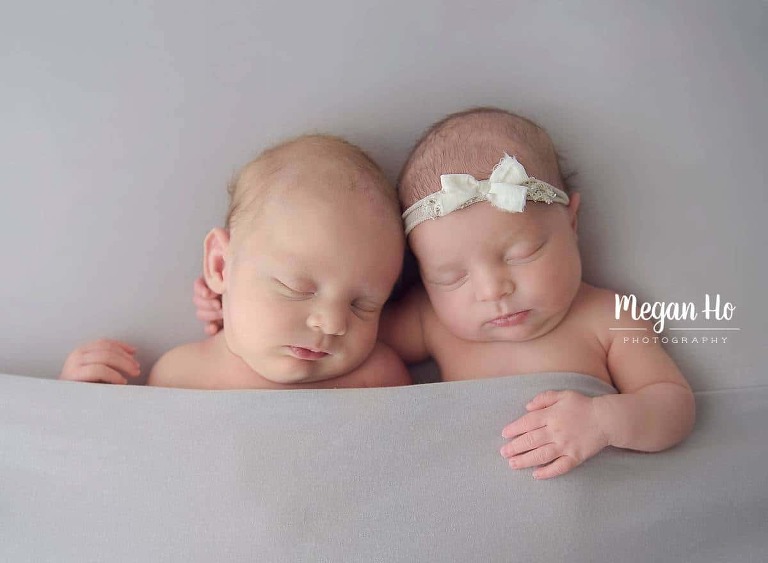 adorable twins tucked in on grey backdrop snuggling together