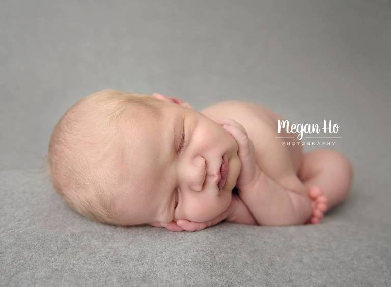 adorable sleeping newborn boy with hands on cheeks on grey backdrop in nh