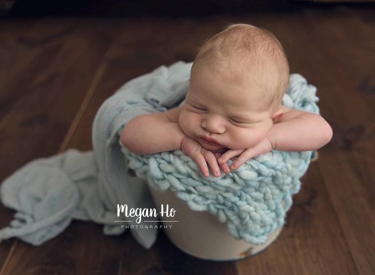 sleeping newborn boy in bucket with chubby cheeks resting on hands in southern nh