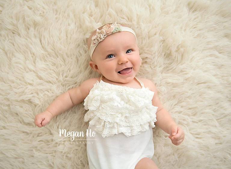 happy four month girl in white romper and headband on white furry rug in nh