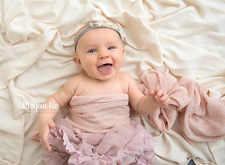 milestone session baby girl with tongue out laying on fabric in pink