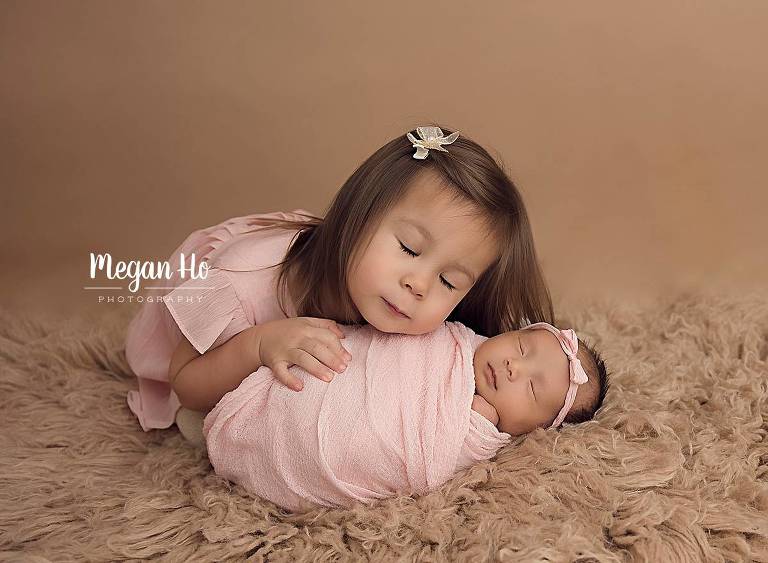 nh big sister cuddling with wrapped newborn both dressed in pink