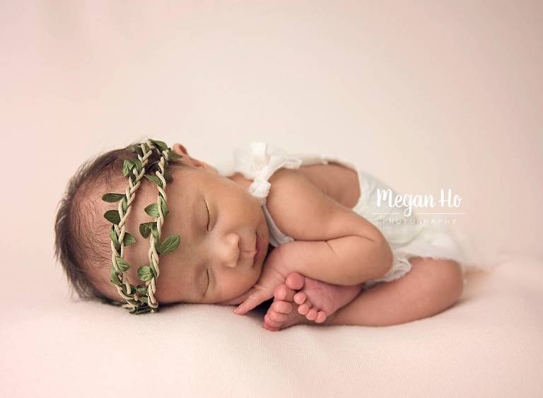 curled up baby girl with green halo and adorable white romper sweetly sleeping with tiny toes showing