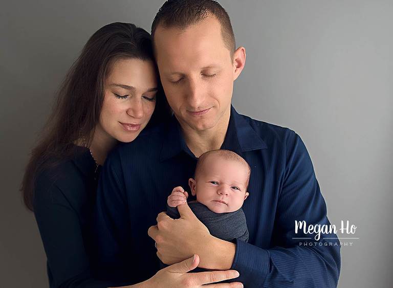 sweet family snuggling their baby boy in navy blue on grey background