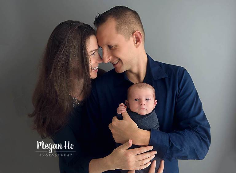 southern nh family smiling hugging their newborn baby boy in navy blue on grey backdrop