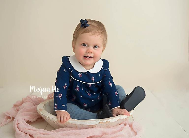 one year girl sitting in while bowl with pink and navy on cream backdrop in nh