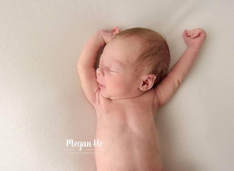 newborn boy sleeping stretching arms up in natural pose on cream blanket