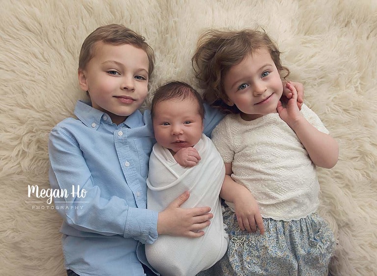 big brother and big sister snuggling with baby brother on white fluffy rug in nh