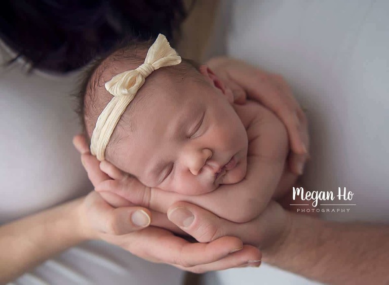 baby girl alseep in mom and dads hands during nh newborn session