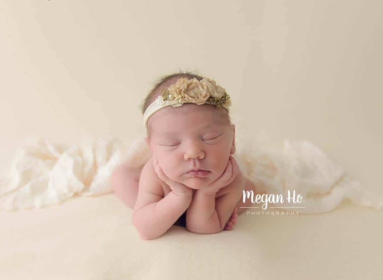 beautiful sleeping newborn on cream with flower headband in froggy pose