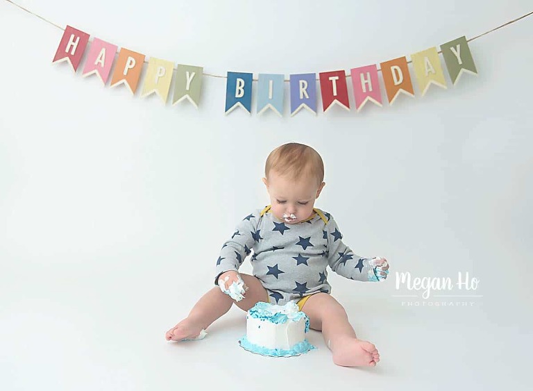 little boy smashing into cake in star onesie with birthday banner