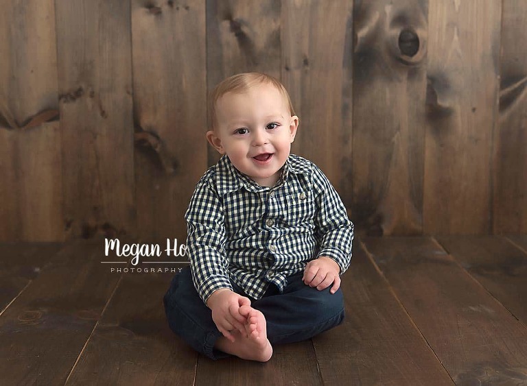 happy one year old boy sitting up on wood floor holding toes