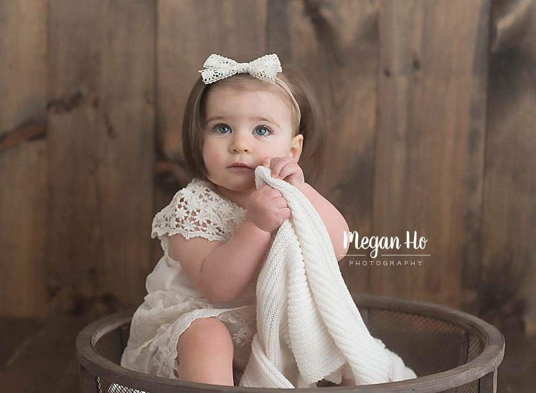 one year girl in white with white bow sitting in wooden bowl in NH studio session