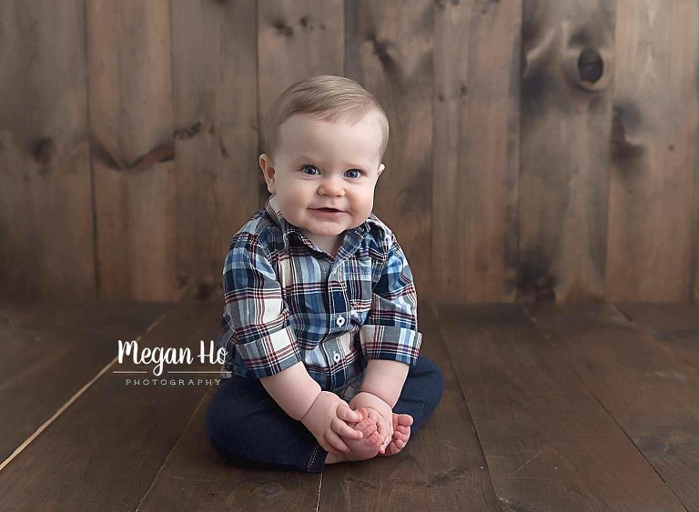 blonde boy sitting on wood in plaid shirt holding his toes