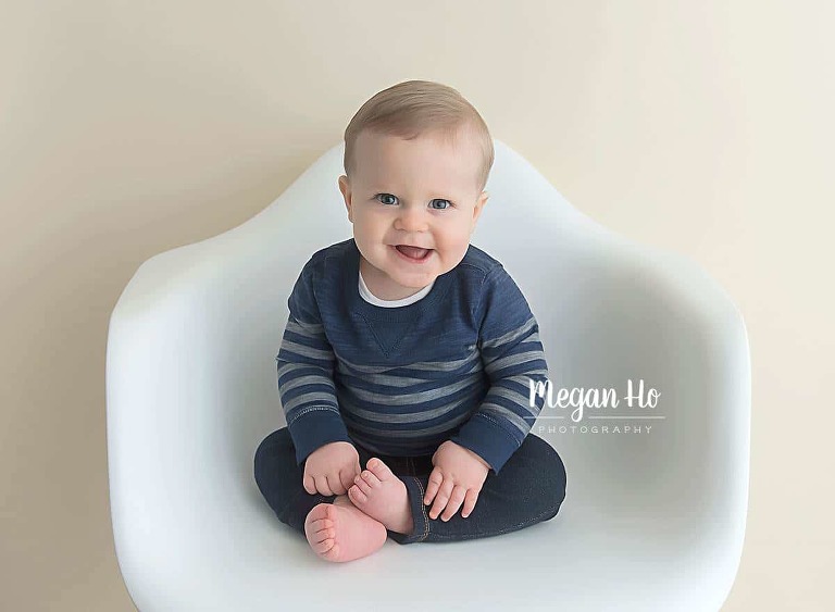adorable smiling boy sitting on white chair in blue in one year studio session